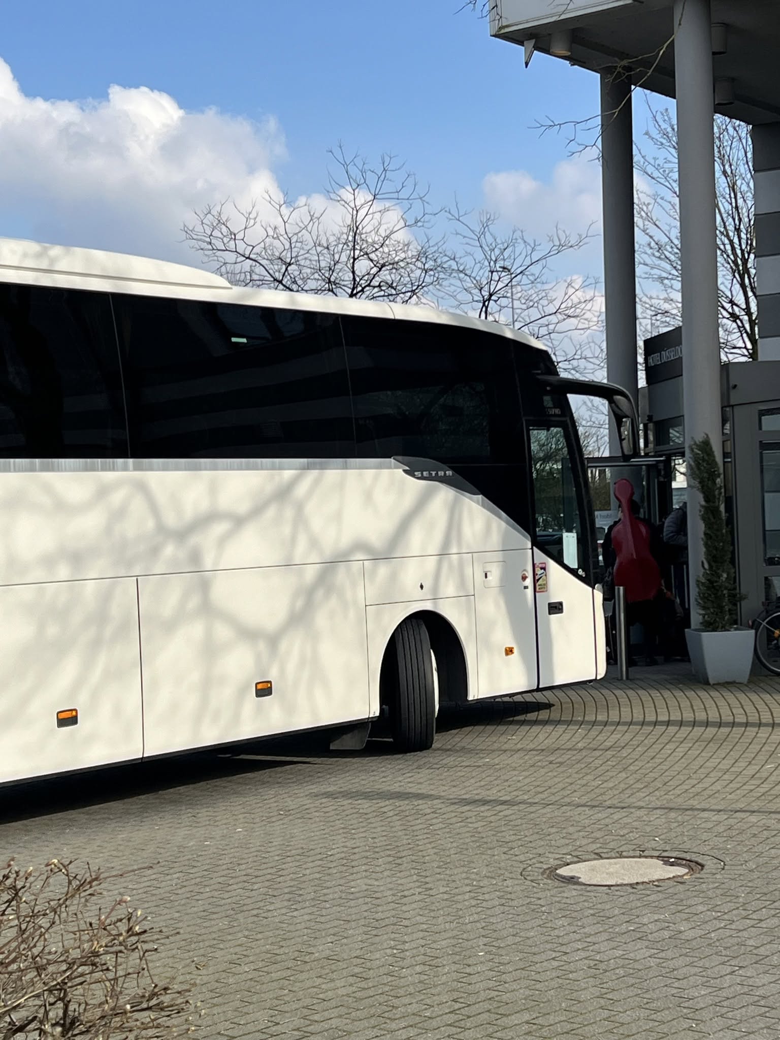 Tour coach at hotel entrance, musician with double bass boarding